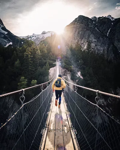 A hiker crossing a rope bridge between mountain cliffs